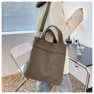Deep olive nylon tote bag shown in a lifestyle setting with adjustable shoulder strap