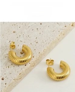 Close-up of golden ribbed U-shape hoop earrings on a textured stone display stand