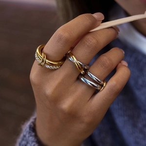 Close-up of stacked bicolor stainless steel rings with knotted and crystal pave designs