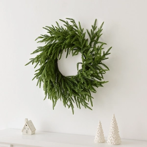 Green Norfolk pine Christmas wreath hanging on a white wall for festive holiday decoration