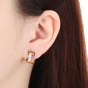 Macro view of C-shaped gold hoop earrings with red and white rhinestones on ear