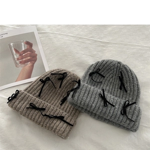 Detail of grey and coffee knit beanies with black bow accents on a grid texture