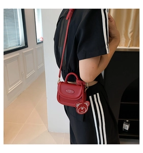 Detailed shot of a mini red crossbody bag with a cute bear pendant worn by a model