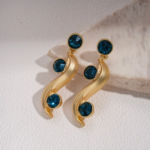 Close-up of golden S-curve vintage earrings with three round deep blue gemstones