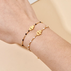 Detail of gold Hamsa Hand bracelet with black and white enamel beads on model's wrist