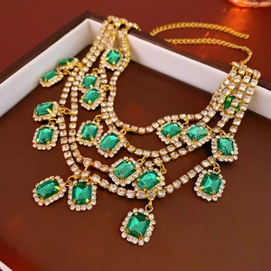 Macro shot of tiered gold necklace featuring emerald stones and cascading tassels