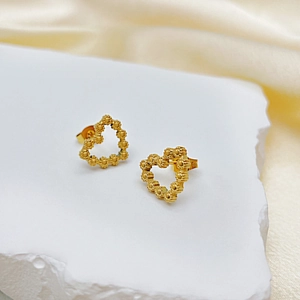 Détail de boucles d'oreilles cœur dorées avec texture perlée sur fond de soie élégant