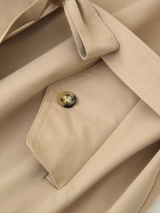 Detailed close-up of khaki twill trench coat featuring tortoiseshell button and belted waist