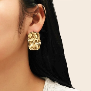 Détail d'une boucle d'oreille rectangulaire dorée avec texture martelée irrégulière