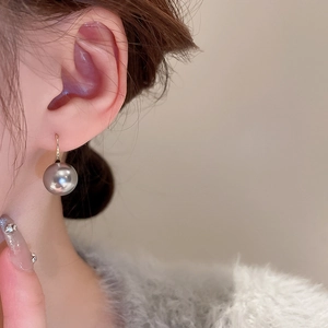 Close-up of elegant pearl drop earring with golden hook worn on a model's ear