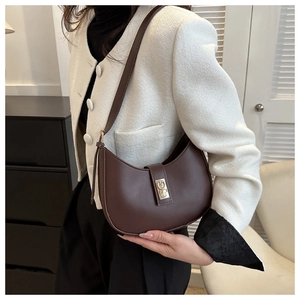 Detail view of a dark brown leather hobo bag with a gold buckle worn on the shoulder