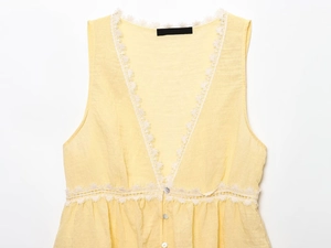 Detailed macro view of delicate white lace trim and pearl buttons on a yellow summer top