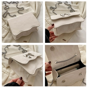 Detail view of white crossbody bag with wavy flap, silver bow and metal chain strap