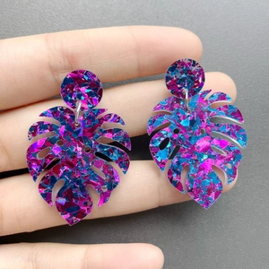 Close-up of monstera leaf earrings with vibrant purple and blue shimmering sequins
