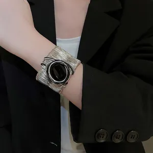 Modern wide silver metal cuff bracelet with black oval centerpiece over a black suit