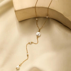 Detail of gold Y-shaped necklace with white pearls on a minimalist stone backdrop
