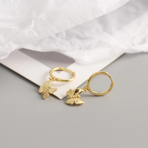 Detailed close-up of golden butterfly charm hoop earrings on a clean minimalist background