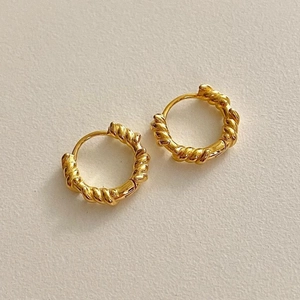 Close-up of small golden twisted hoop earrings on a textured off-white paper background