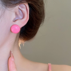 Close-up of a model wearing a glossy hot pink round button earring with a polished finish