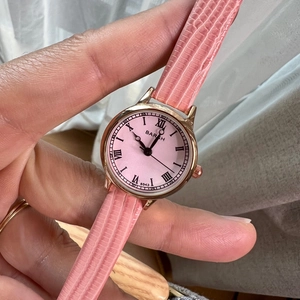 Detailed close-up of a pink small dial watch with Roman numerals and leather strap