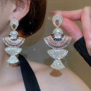 Close-up of golden fan-shaped earrings with colorful sparkling crystals on ear
