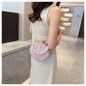 Pink sequin shell handbag with pearl handle and gold chain strap shown on a model