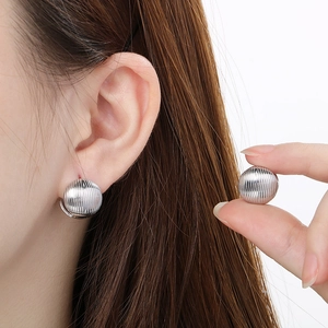 Macro detail of silver stainless steel earring featuring a textured striped sphere design