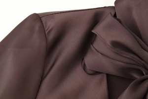 Detailed close-up of dark brown satin dress shoulder with silky fabric texture and bow
