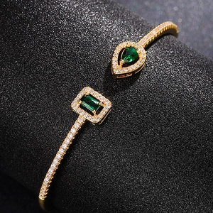 Macro detail of gold-plated open cuff with emerald green and teardrop zircon stones