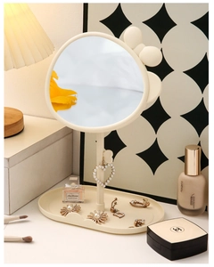 Detail of a beige heart-shaped vanity mirror featuring a functional jewelry storage base
