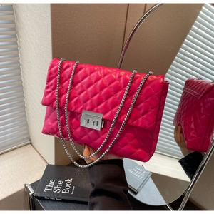 Detail of rose red quilted chain bag with polished metal lock and shiny leather texture