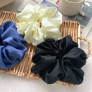 Oversized satin silk hair scrunchies in blue, beige, and black on a woven tray