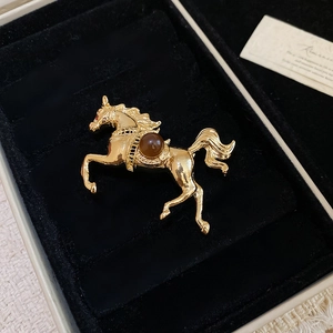 Detail of a gold horse brooch with a brown resin bead in a black velvet gift box