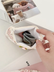 Gros plan de la mini pochette fleurie en dentelle contenant rouge à lèvres et cartes