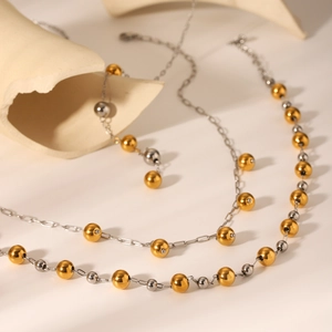 Two-tone gold and silver stainless steel beaded necklace shown on a ceramic prop