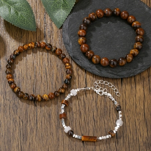 Tiger eye stone bead bracelets and silver cuboid charm wristbands on a dark wood table