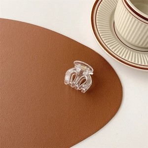 Detail of small clear acrylic hair claw clip with gold spring on a leather mat