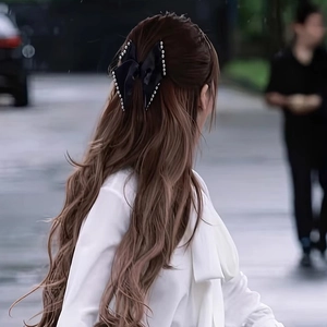 Detailed view of the black satin bow hair claw with pearl trim on a half-up hairstyle