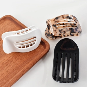 Close-up of three acetate hair claws in white, tortoiseshell, and black on a wooden tray