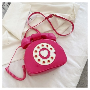 Detail of rose red vintage telephone shaped crossbody bag with heart dial and spring cable