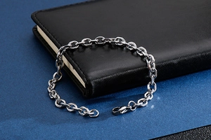 Detail of silver link chain bracelet with lobster clasp on black leather notebook