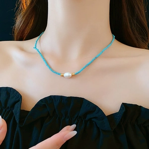 Close-up of turquoise beaded necklace with white pearl and gold accents on a model neck