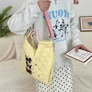 Detail of cute black cat embroidery on quilted pale yellow tote bag shown on a model