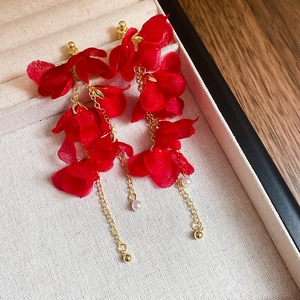 Detailed macro view of red flower tassel earrings with golden chains and pearls