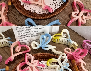 Detail view of large gradient bow hair claws in pink, blue, yellow on a lace mat
