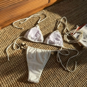 Flat lay of white halter bikini with decorative shells and beads on a woven beach mat