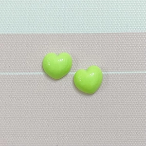 Macro shot of two glossy lime green resin heart charms on a textured striped fabric