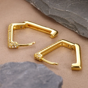 Detail of 18k gold plated square hoop earrings with cubic zirconia on beige fabric