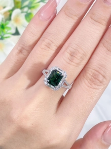 Close-up of emerald-cut green gemstone ring with pavé diamond halo on silver band