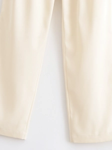 Detail view showing beige high-waisted trousers with premium fabric texture and clean hems